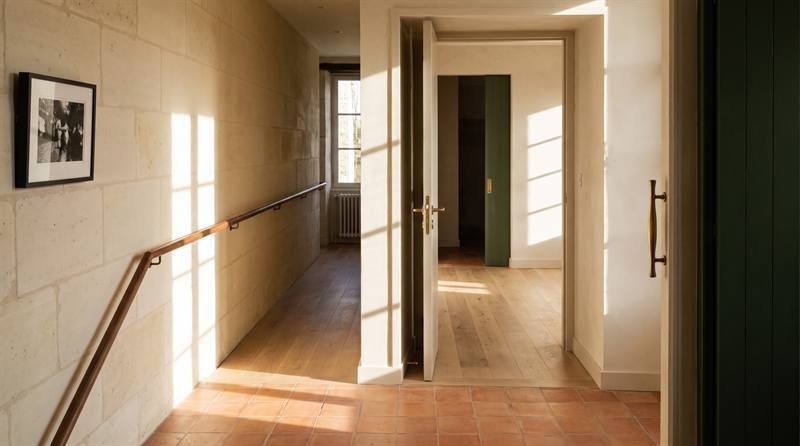 Couloir élargi sans seuil, avec main courante en bois continue et porte à poignée béquille.